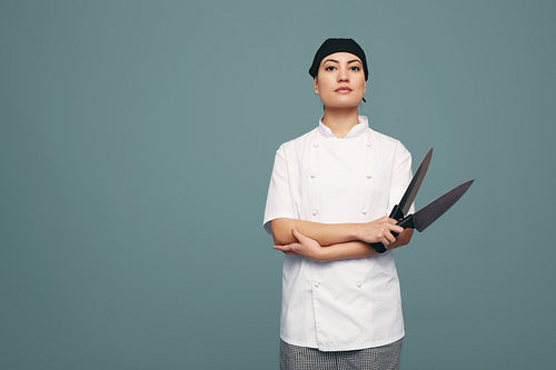 Female culinary chef holding two kitchen knives in a studio