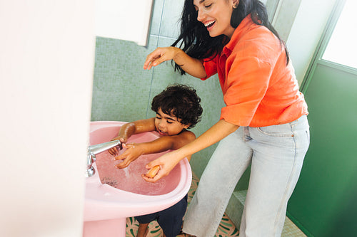 Mother helping child wash hands in colorful bathroom with pink sink