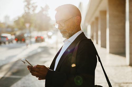 Mature businessman using smartphone outdoors in urban environment during workday