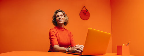 Mature woman providing customer support in vibrant monochrome orange office setting with copy space
