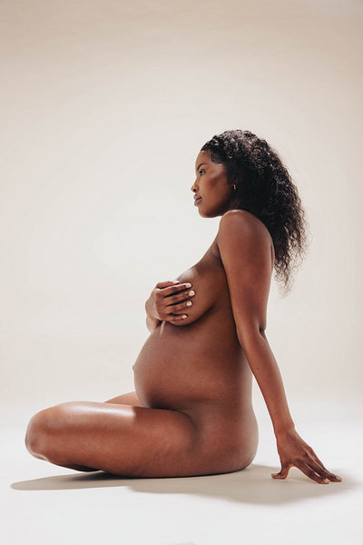 Naked, dark-skinned pregnant woman embracing her maternity body in studio