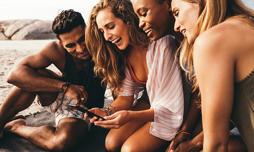 Group of friends sitting at the beach having fun