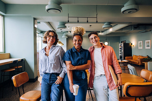 Three young adults smiling together in a casual office setting