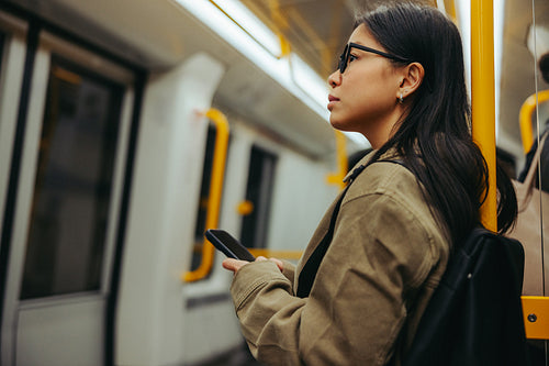 Woman commuter on subway looking out with phone