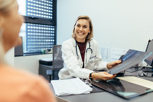 Smiling doctor holding x-ray communicating with patient