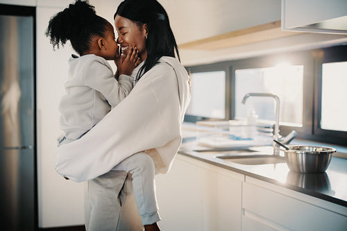 Daughter kisses her mom as she sits in her arms on mother’s day