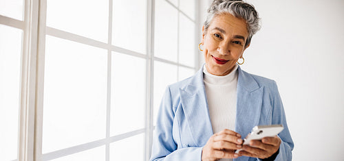 Business woman holding a smartphone and looking at the camera in an office