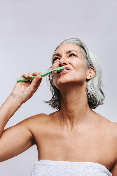 Mature woman brushing her teeth in studio feeling confident