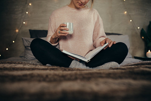 Woman reading book on bed at home