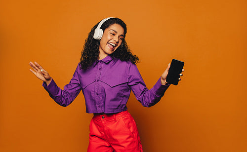 Happy woman dancing to music with headphones on a vibrant orange background