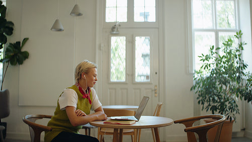 Waving woman joins a laptop video call in a cafe workspace