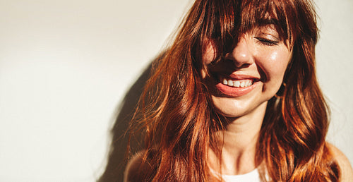 Woman with red hair smiling while standing against a wall