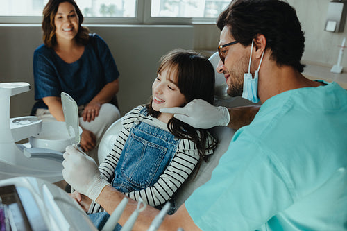 Dentist uses mirror to explain dental procedure to smiling child patient