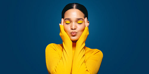 Radiating self-love: Young woman with colourful makeup embraces her face in a studio