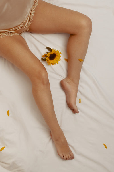 Woman having a sensual moment in a sunflower-themed boudoir, dressed in nightwear and sitting on white bed sheets