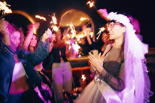 Bride-to-be celebrates surrounded by happy friends with sparklers at a party