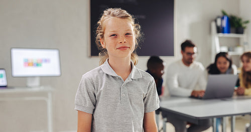 Male student looking at the camera in a digital literacy classroom, with his teacher and classmates coding in the background