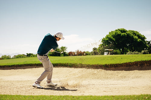 Male golfer skillfully showcasing athletic game techniques and concentration escaping sand bunker