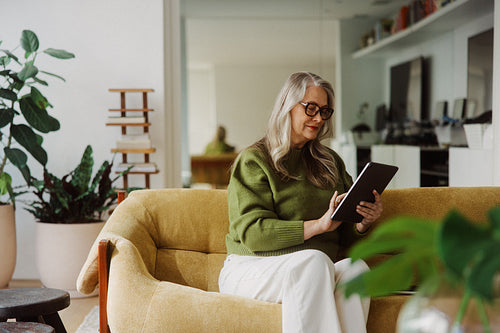 Browsing senior woman uses a tablet on the sofa
