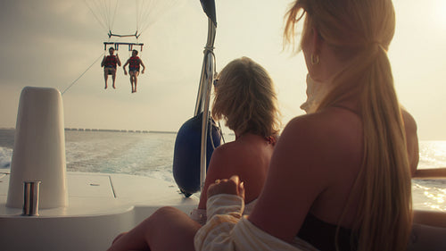 Friends on a boat watching people parasailing over the ocean at sunset