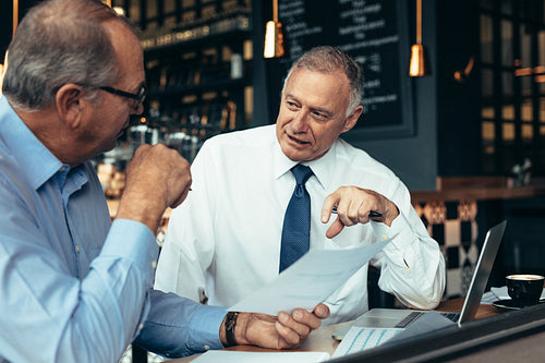Men discussing business reports at cafe