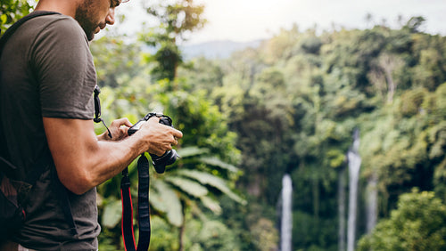 Young man with camera by a waterfall in forest