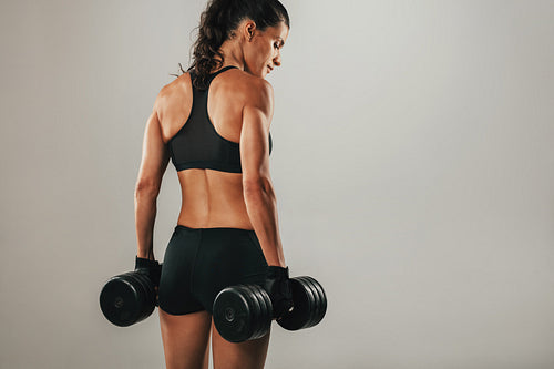 Back of beautiful woman holding dumbbells