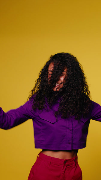 Young woman dancing enthusiastically and laughing on yellow background