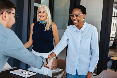 Three individuals in an office greeting each other with smiles and handshakes