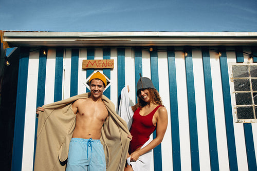 Playful friends outside striped sauna bathhouse for wellness ritual