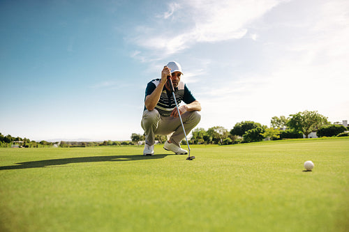 Close up of a focused male golfer lining up a putt on a scenic golf course