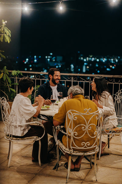 Family dining outdoors under string lights at night with happy conversations