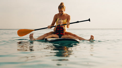 Mother teaching child to balance on paddle board during watersport activity