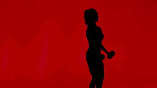 Silhouette of a strong female athlete performing a dynamic fitness workout with dumbbells