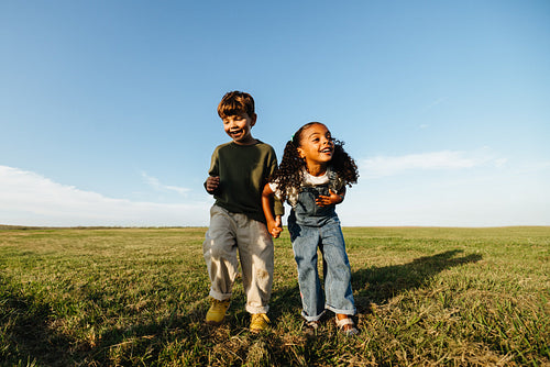 Young boy and girl run across open field together.