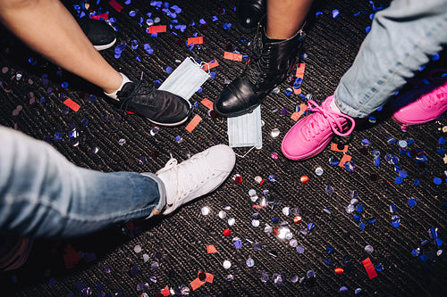 Unrecognizable people stepping on face masks and confetti