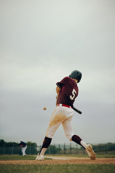Baseball player in uniform swinging bat during game as ball approaches the batter's box