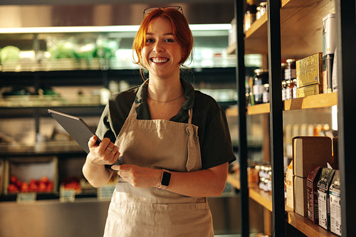 Happy young grocery store owner smiling at the camera in her shop