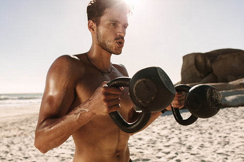 Man doing fitness training at the beach using kettlebells