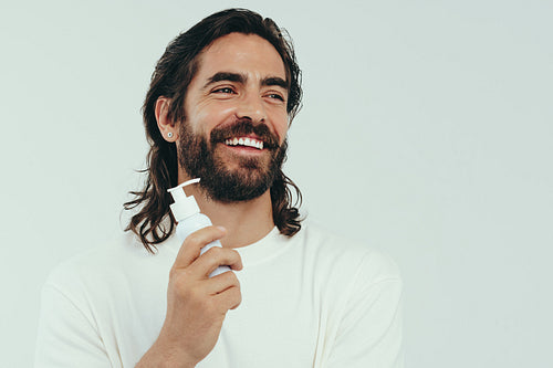 Man with a beard looking happy while holding a skin cleanser product in a studio