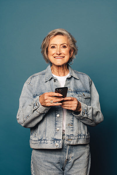 Fashionable woman smiling and holding smartphone app in studio portrait