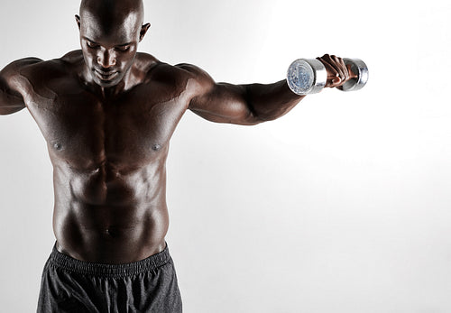 Male model exercising with dumbbells on grey background