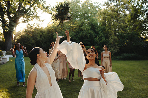 Women celebrating during a bouquet toss at an outdoor wedding