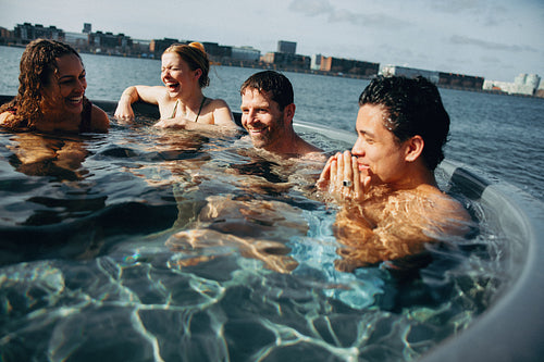 Friends relax in outdoor hot tub spa by waterfront city skyline