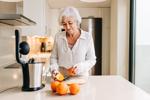 Happy senior woman making fruit juice using an electric blender