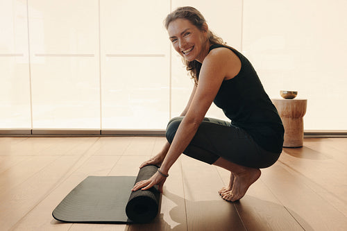 Healthy senior woman rolling up an exercise mat at home