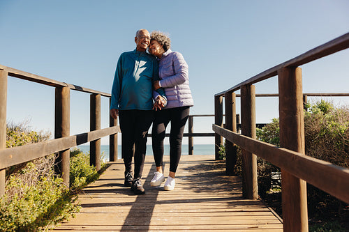 Senior couple walking along a wooden foot bridge at the beach