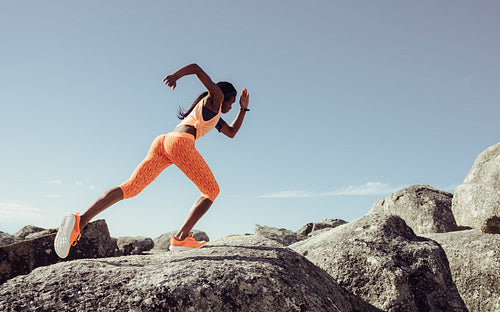 Female runner running over big rocks