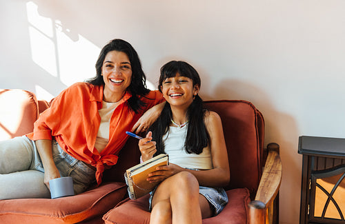 Cheerful Latin American mother and daughter sitting together in a cozy home setting