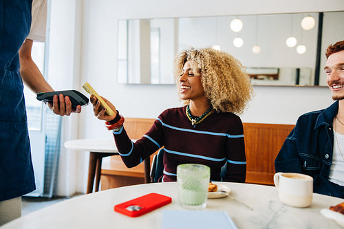 Young woman making mobile payment with friends at cafe